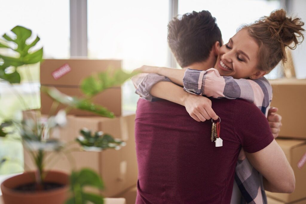 A Young Couple hugging holding the keys to their new home with boxes in the background.